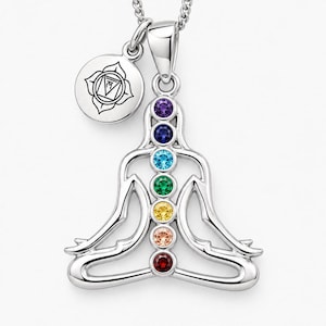 Könnte beinhalten: Ein silberner Anhänger in Form einer sitzenden Meditationsfigur mit sieben vertikal angeordneten runden Edelsteinen in Violett, Blau, Hellblau, Grün, Gelb, Pfirsich und Rot. Ein kleiner runder Anhänger mit einer Strichzeichnung ist befestigt.