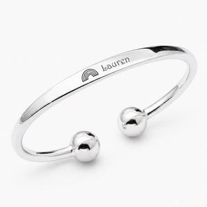 May include: A polished silver-tone cuff bracelet featuring an open design with spherical ends. The outer surface is engraved with a small rainbow icon followed by the name Lauren in a clean, dark script font, creating a simple and elegant accessory.