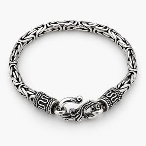 May include: A silver chain bracelet featuring a complex Byzantine weave pattern. The bracelet is secured with a decorative hook clasp that has intricate scrollwork and engraved details on both the clasp and the cylindrical end caps.