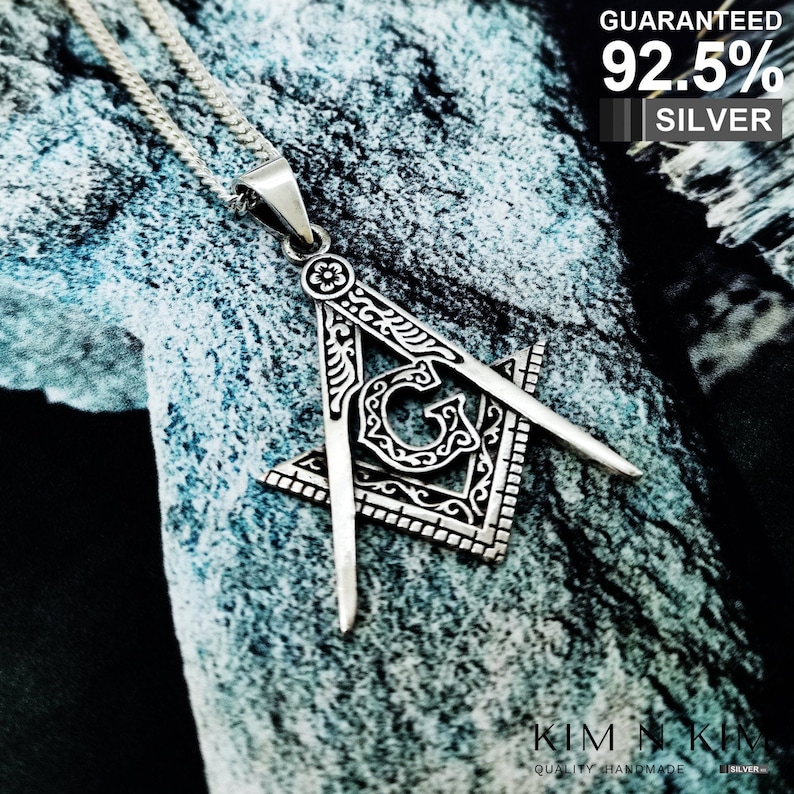 May include: A silver pendant necklace featuring a detailed, ornate silver Masonic compass and square design. The pendant is 92.5% silver, as indicated by the text "Guaranteed 92.5% Silver".