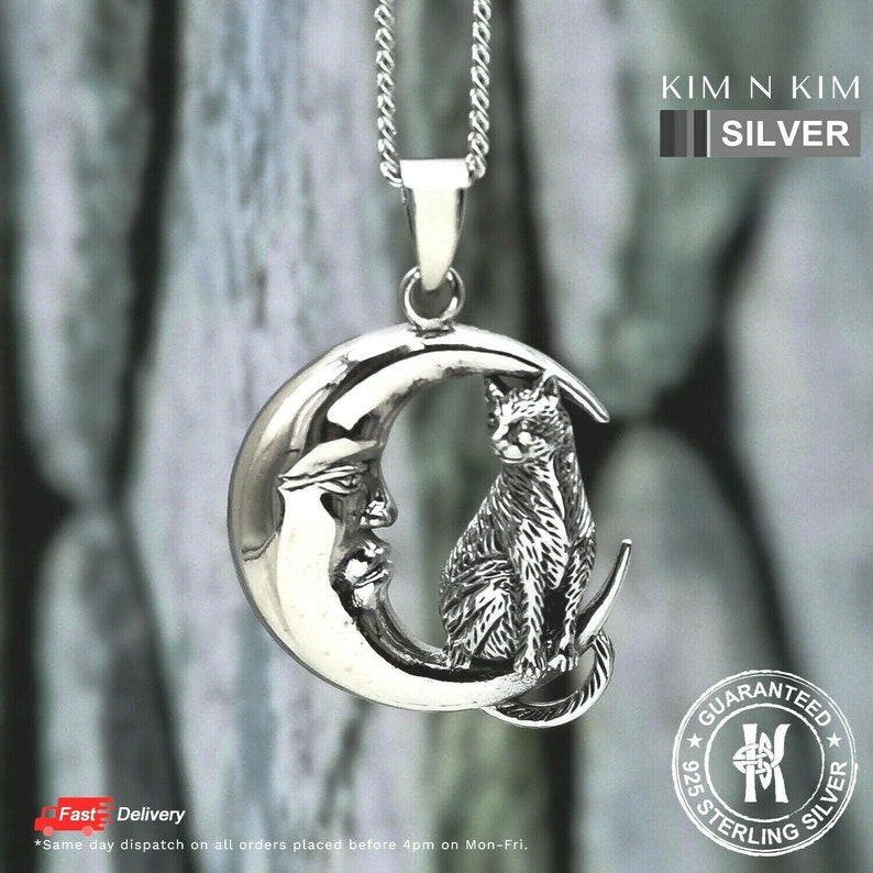 Puede incluir: Un collar con colgante de plata de ley que representa un gato posado en una luna creciente con una cara. El colgante cuelga de una delicada cadena. El texto "KIM N KIM SILVER" es visible.