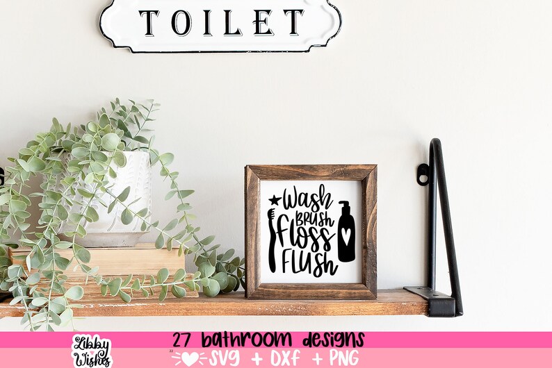 May include: A wooden sign with the text "Wash Brush Floss Flush" in black lettering. The sign is on a shelf with a plant and a sign that says "Toilet".