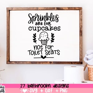 May include: A white sign with black text that reads "Sprinkles are for cupcakes not for toilet seats". The sign is framed in a brown wood frame. There is a cupcake illustration with a heart below the text.