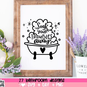 May include: A black and white illustration of a bathtub with bubbles and the text "Soak your troubles away". The illustration is framed in a wooden frame and displayed on a white wall with a potted lavender plant in the foreground.