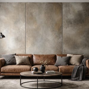 Könnte beinhalten: Ein braunes Ledersofa mit vier Kissen in Grau- und Beigetönen sowie einer dunkelgrauen Decke, die über eine Armlehne drapiert ist. Ein runder Couchtisch aus Holz steht davor und trägt zwei schwarze Vasen und einen Stapel Bücher.