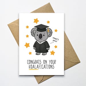 May include: A graduation greeting card featuring a cartoon koala wearing a graduation cap and gown, surrounded by yellow stars. The card reads "Congrats on your Koalafications" with the phrase "that's you!" in a speech bubble.