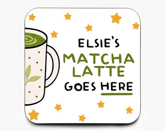 May include: A square coaster with rounded corners. It features a matcha latte design with a white background, gold stars, and a green matcha latte mug. Text on the coaster reads "Elsie's Matcha Latte Goes Here."