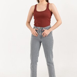 Puede incluir: Una mujer con un top de tirantes de color &oacute;xido con textura de canal&eacute; y unos vaqueros rectos de color gris claro. Est&aacute; de pie con las manos en los bolsillos y lleva sandalias de tac&oacute;n beige.