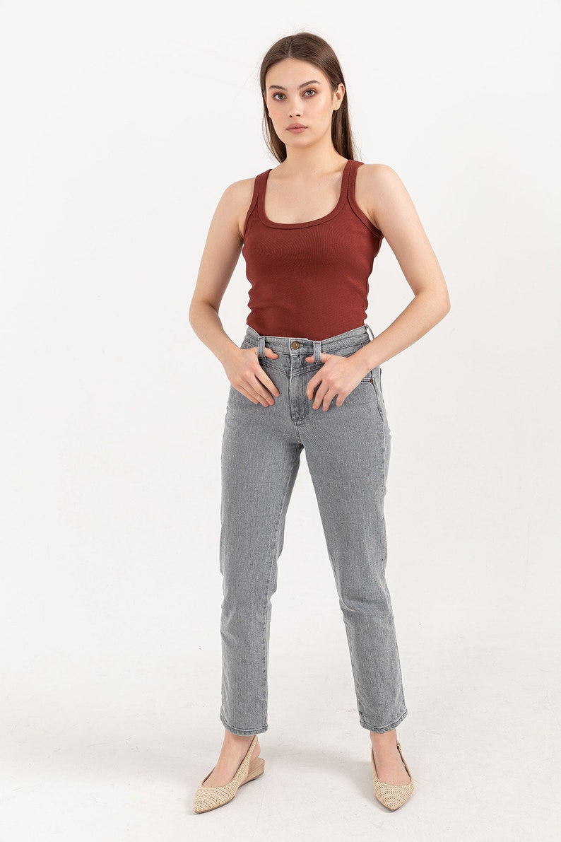 Puede incluir: Una mujer con un top de tirantes de color &oacute;xido con textura de canal&eacute; y unos vaqueros rectos de color gris claro. Est&aacute; de pie con las manos en los bolsillos y lleva sandalias de tac&oacute;n beige.