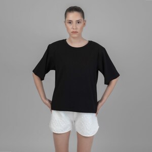 May include: A black short-sleeved t-shirt with a crew neck and white shorts. The model is wearing the shirt and shorts.