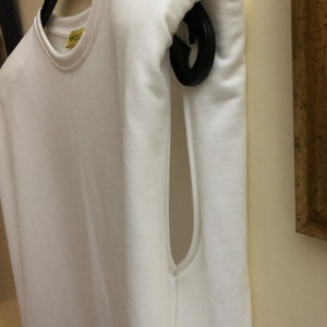 May include: White sleeveless shirt with a yellow tag that says "HOS" hanging on a black hanger.