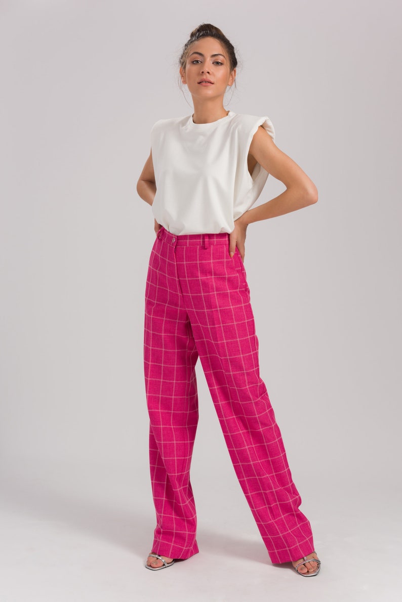 May include: A woman is wearing a white sleeveless top with padded shoulders and pink plaid wide-leg pants.