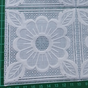 May include: White lace doily with a floral design. The doily is made of delicate, intricate lace and features a repeating pattern of flowers and leaves. The doily is perfect for adding a touch of elegance to any table setting.