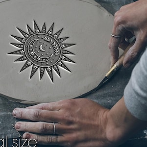 Peut inclure: Une pièce d'argile grise claire avec un motif de soleil et de lune est en cours de sculpture. Le motif comprend un soleil, un croissant de lune et des étoiles. Le texte "Not real size" et "Size depends on your choice" est en bas.
