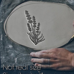 May include: A gray clay slab with a detailed black floral design of lavender. The text "Not real size. Size depends on your" is at the bottom of the image. A hand is visible, holding the clay.