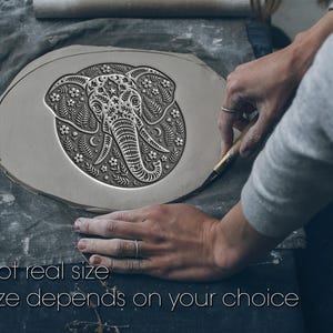 May include: A gray ceramic elephant design with floral and star patterns is being carved. The elephant is centered on a round, oval-shaped piece of clay. The text "Not real size" and "Size depends on your choice" is at the bottom of the image.