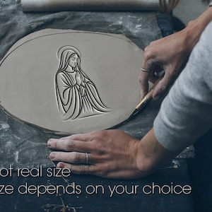 Może przedstawiać: Jasnoszary kawałek gliny z wygrawerowanym wizerunkiem postaci religijnej. Postać ma na sobie szatę i aureolę. Tekst "Not real size" i "Size depends on your choice" znajduje się na dole obrazu.
