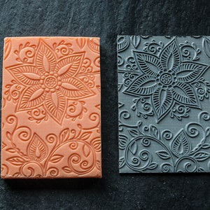 May include: Two silicone baking mats with intricate floral designs. One mat is orange and the other is gray.