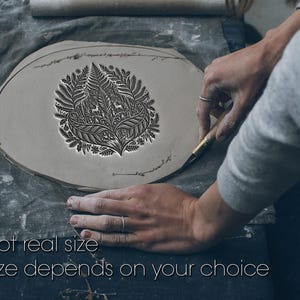 May include: A flat, circular piece of grey clay featuring a detailed, embossed botanical design with ferns and two small deer figures. A tool is being used to trim the edge of the clay. The text "Not real size. Size depends on your choice" is visible.