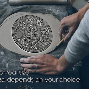May include: A detailed, silver-colored ceramic plate with an intricate floral and celestial design is being crafted. The plate features moons, flowers, and other botanical elements. The text "Not real size" and "Size depends on your choice" is visible.