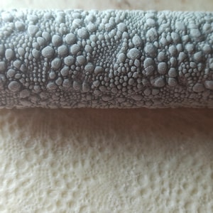 Può includere: Un mattarello grigio con una superficie testurizzata di piccoli cerchi in rilievo. Il mattarello viene utilizzato per creare un motivo decorativo sui prodotti da forno.