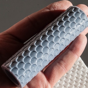 May include: A grey silicone rolling pin with a textured surface that resembles fish scales. The rolling pin is approximately 15 cm long.