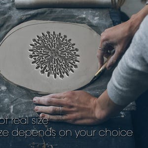Puede incluir: Una pieza de arcilla gris claro con un diseño floral está siendo trabajada. El texto "Not real size" y "Size depends on your choice" es visible. La arcilla está sobre una superficie de tela gris.