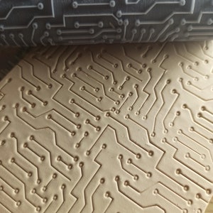 May include: A close-up of a gray silicone roller with a raised circuit board design. The roller is used to create an imprint of the design on a surface.