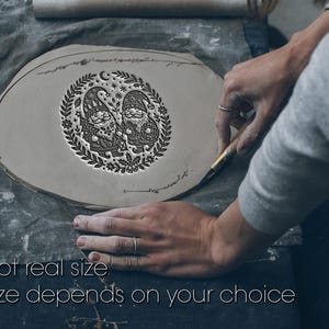 Può includere: Un pezzo di argilla grigia, piatto e circolare, con un design profondamente impresso di due gnomi circondati da una ghirlanda di foglie, stelle e bacche. Il testo "Not real size. Size depends on your choice" è visibile in basso.