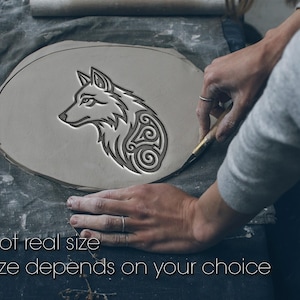 May include: A light gray clay piece with a wolf design is being carved. The wolf profile features intricate patterns. The text "Not real size" and "Size depends on your choice" are at the bottom. The clay is on a gray cloth.