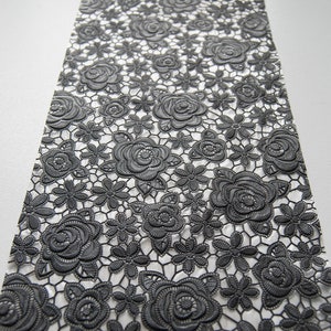 Peut inclure: Tissu de dentelle noire avec un motif floral délicat composé de roses et de petites fleurs. La dentelle est translucide et présente une texture légèrement en relief.