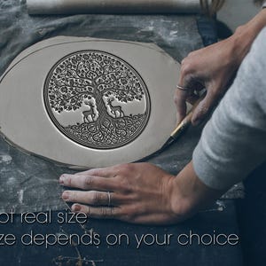Może przedstawiać: Jasnoszary, owalny ceramiczny element z szczegółowym wzorem drzewa życia, w tym jelenie. Tekst "Not real size" i "Size depends on your choice" znajduje się na dole. Osoba pracuje nad elementem.