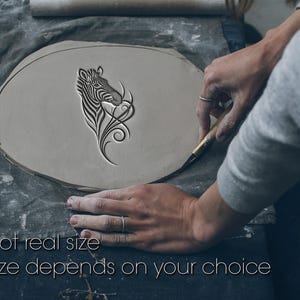 Peut inclure: Une pièce d'argile gris clair avec un motif de zèbre sculpté. Le zèbre a des rayures noires et blanches et est entouré de volutes décoratives. Le texte "Not real size. Size depends on your choice" est en bas.