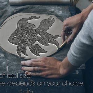 May include: A grey ceramic piece featuring a detailed goldfish design is being carved. The fish has scales, fins, and a flowing tail. The text at the bottom reads "Not real size. Size depends on your choice."