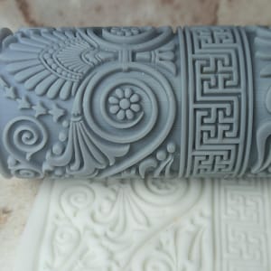 Peut inclure: Rouleau à pâtisserie gris avec un motif décoratif de volutes, d'étoiles et de clé grecque. Le rouleau à pâtisserie est utilisé pour créer un motif en relief sur le fondant ou la pâte.