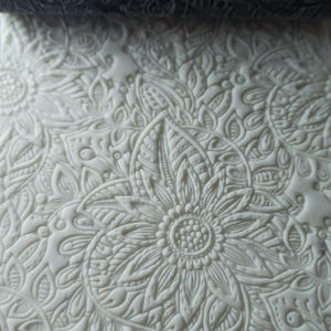 Può includere: Fondant bianco in rilievo con un motivo floreale dettagliato. Il design presenta un grande fiore al centro circondato da fiori e foglie più piccole.