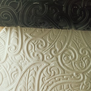 Puede incluir: Primer plano de una superficie blanca texturizada con un patrón repetitivo de remolinos y hojas. La superficie parece haber sido estampada con un rodillo.