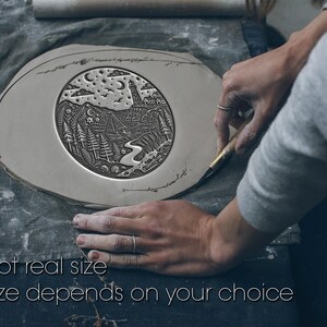 May include: A circular clay slab featuring an intricate embossed landscape design of a lighthouse, a sailboat on water, pine trees, and a starry night sky. The relief carving shows detailed textures of waves, clouds, and foliage on a flat surface.