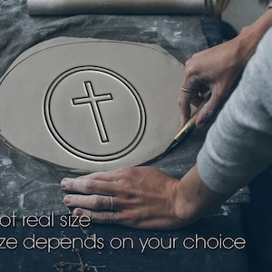 Könnte beinhalten: Ein hellgraues Tonstück mit einem Kreuzdesign in einem Kreis wird mit einem Werkzeug geschnitten. Der Text "Not real size" und "Size depends on your choice" steht unten. Der Ton liegt auf einem grauen Tuch.
