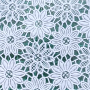 May include: White lace fabric with a repeating pattern of delicate floral designs. The fabric has a fine, open weave and a soft, airy feel.