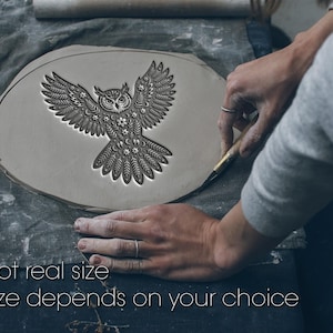 May include: A detailed owl design is carved into a gray clay disc. The owl has outstretched wings and intricate patterns. The text "Not real size" and "Size depends on your choice" is at the bottom. The image shows a craft in progress.