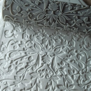 May include: A gray rolling pin with a floral design. The rolling pin is used to create an embossed pattern on dough or fondant.