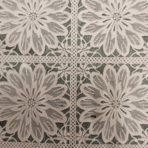 May include: White lace tablecloth with a repeating floral pattern. The tablecloth has a delicate, intricate design.