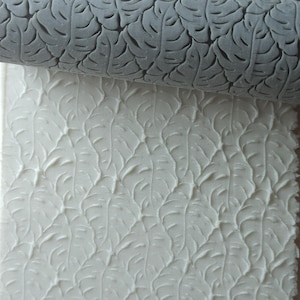 May include: A gray rolling pin with a leaf pattern design. The rolling pin is used to create an embossed leaf pattern on a white surface.