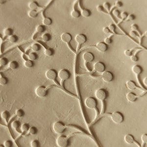 May include: Close-up of a light beige textured surface with a repeating pattern of embossed floral sprigs. The sprigs have small round buds and delicate stems.