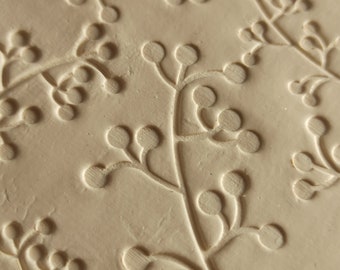 May include: Close-up of a light beige textured surface with a repeating pattern of embossed floral sprigs. The sprigs have small round buds and delicate stems.