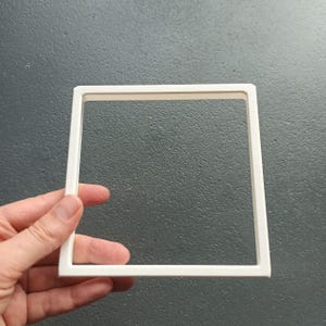 Può includere: Una cornice quadrata bianca con una superficie piatta e liscia e un centro vuoto. La cornice presenta bordi dritti e puliti e uno spessore uniforme, costruita in materiale solido con finitura opaca, presentata come un semplice bordo geometrico.