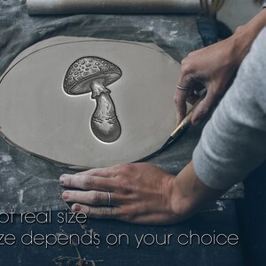 May include: A gray clay slab featuring a deeply embossed, detailed illustration of a mushroom with a textured cap and stem. The text "Not real size. Size depends on your choice" is printed in white at the bottom of the image.