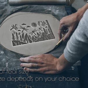May include: A light gray clay piece with a nature-themed design, including trees, dragonflies, and a sun. The text "Not real size" and "Size depends on your choice" is visible. The clay is being worked on by a person.