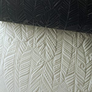 May include: A close-up of a white textured surface with a repeating pattern of embossed feathers. The surface is smooth and has a subtle sheen.